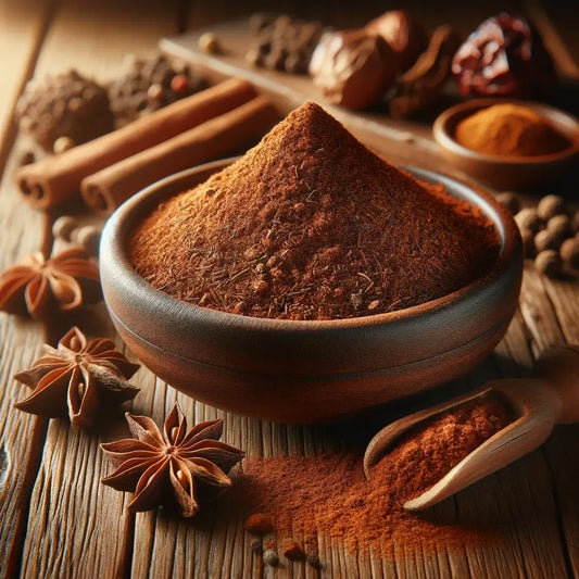 A bowl of Ras el Hanout spice blend surrounded by star anise, cinnamon sticks, and other aromatic spices on a wooden table.